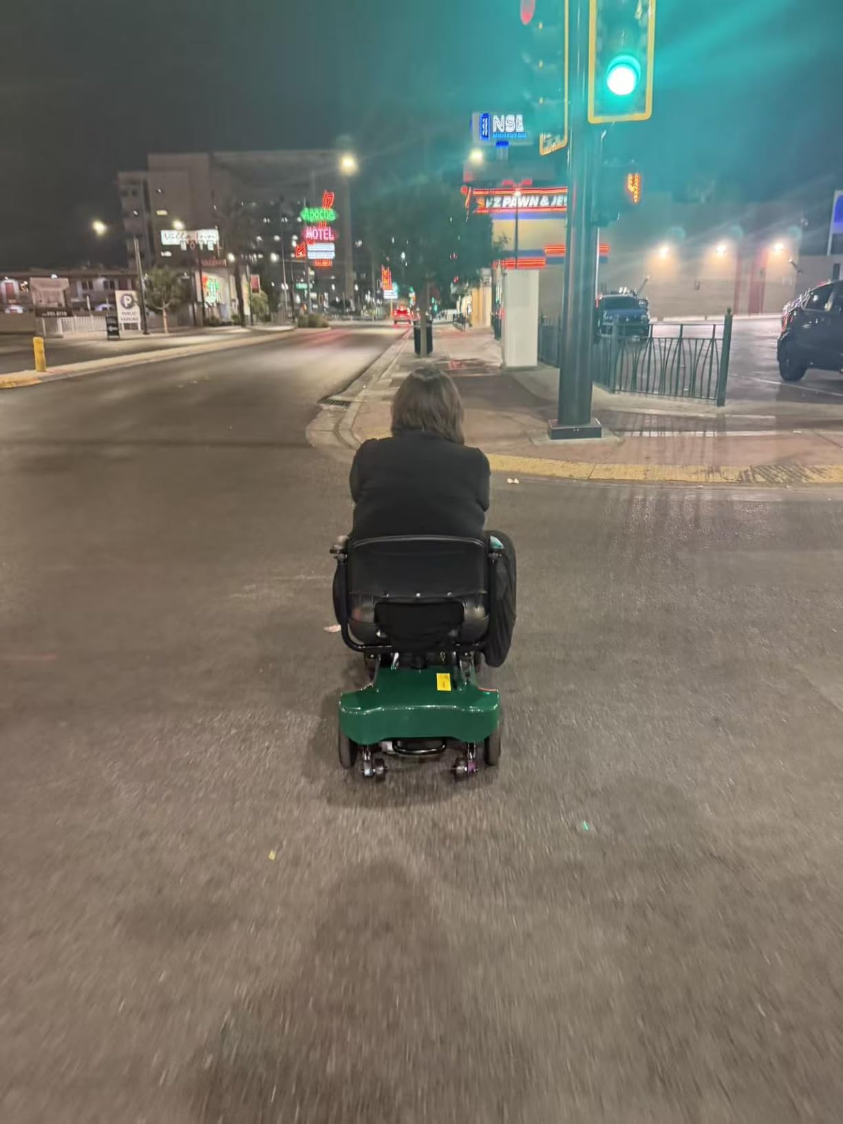 Customer riding the scooter across a city street at night